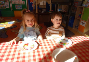Dwóje dzieci z uśmiechniętymi buziami obserwują jak powstaje tęcza a talerzu.